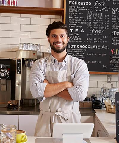 Ventajas para Autonomos - El dueño de una cafeteria  con los brazo cruzados sonriendo tras la barra de su negocio